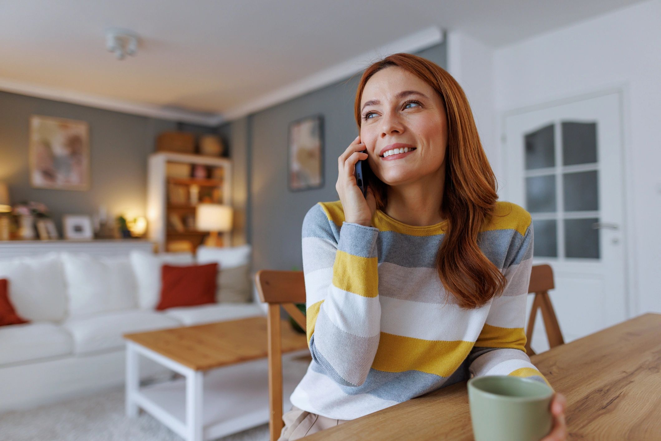 Smiling woman talking on phone and drinking coffee at home
